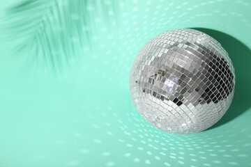 Disco ball with palm leaf shadow on turquoise background