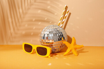 Disco ball with sunglasses, starfish and straws on color background