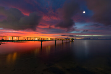 A vivid sunset reflects off the still ocean waters at the Fish Eye Underwater Observatory pier as...