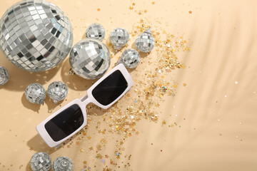 Disco balls with sunglasses and confetti on beige background