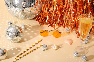 Disco balls with glass of champagne, seashells and sunglasses on beige background