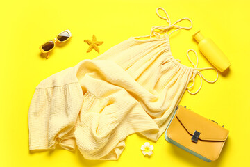 Female summer dress with sunglasses, sunscreen and handbag on yellow background