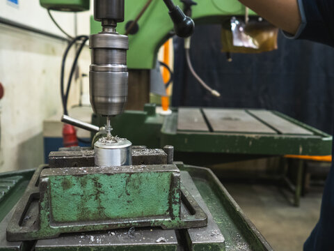 Close-up of metal drilling process using an industrial drill press machine in workshop. worker wearing protective gloves securing the workpiece in vise, demonstrating precision machining and safety