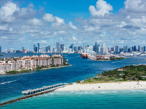 Aerial view of South Pointe Beach, Fisher Island, and Downtown Miami skyline under blue sky. c.