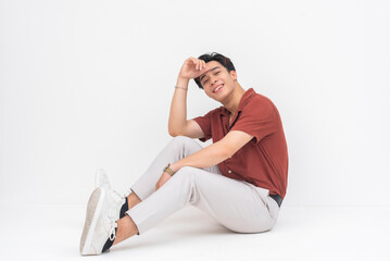 A charming young Asian man sitting on the floor in a relaxed pose, gently placing his hand on his...