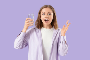 Surprised young woman with glass of water on lilac background