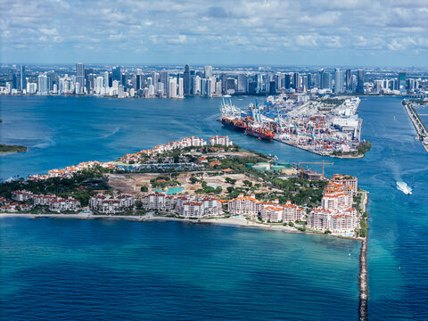 Aerial view of South Pointe Beach, Fisher Island, and Downtown Miami skyline under blue sky. c.
