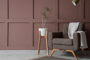 Comfortable armchair, floor lamp and houseplant near brown wall in interior of living room, closeup