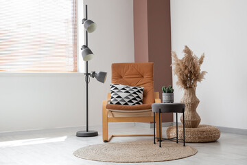 Fototapeta premium Comfortable armchair, floor lamp and vase with pampas grass near white wall in interior of living room
