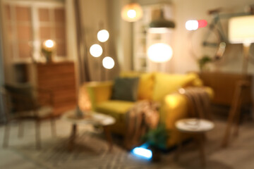 Blurred view of living room with yellow sofa, armchair and glowing lamps in evening