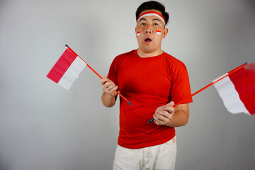 Portrait a proud Indonesian man wearing red with flag face paint and headband holds and waves two...