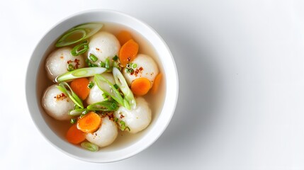 Top-down view of fish ball soup with sliced carrots and scallions in white bowl.
