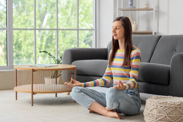 Young woman meditating on carpet at home