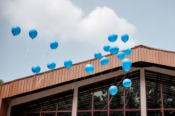 A cluster of blue balloons drifting into a partly cloudy sky above a modern building, symbolizing...