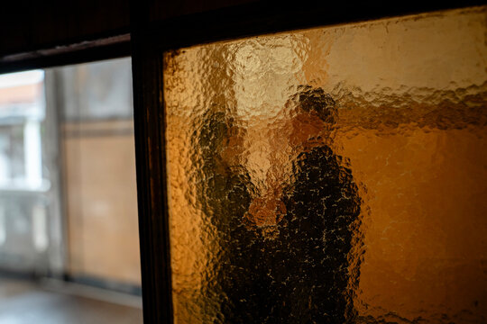 Silhouette of a couple captured through a textured, amber-colored glass pane, creating a warm, intimate, and mysterious mood of togetherness.
