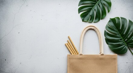 A natural jute bag filled with bamboo straws, adorned with lush green monstera leaves on a textured gray background