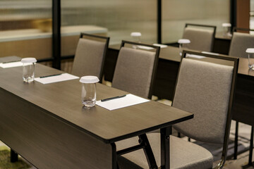 Empty meeting room prepared for a conference or seminar. A glass of water, notepad, and pen are set on a dark wood table before the event begins.