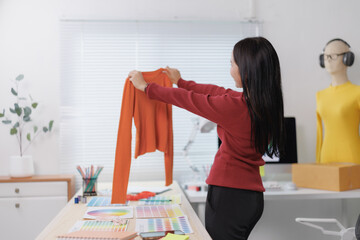 Fashion designer holding orange long sleeved shirt in her studio