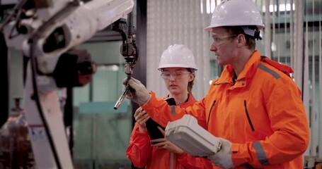 Male and female technicians analyzing welding robot arm programming during slowmotion scene in industry40 lab while calibrating control device for smart automation and training demonstration purpose