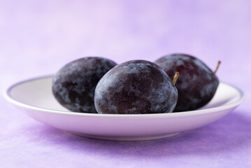 Fresh blue plum fruit on white plate with purple background