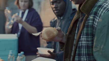 Group of volunteers providing water, bread, beans and pasta to diverse homeless men at food station during community outreach event in city alley - Powered by Adobe