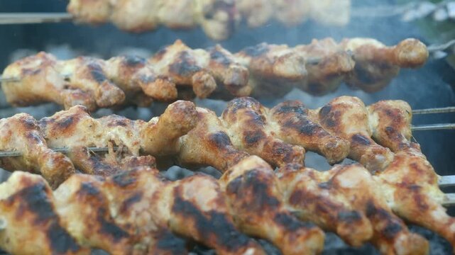 Smoke rises from rows seasoned chicken wings, slowly rotating on metal skewers over hot grill, creating mouthwatering display of sizzling, golden brown goodness. Delicious chicken wings grilling.