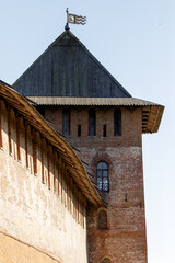 Detailed view of an ancient fortress tower and defensive wall made of red brick, featuring wooden roof and decorative battlements. © Yura Borisov