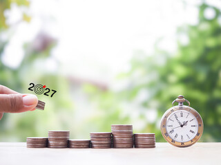 Hand putting coin into stack of coins and vintage watch. The concept of business growth, Financial investment, Market stock, Profit return, Dividend and Business fund in year 2027