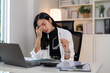 Tired asian businesswoman massaging nose bridge at office desk