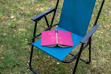 Empty folding chair with book outdoors