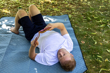 man lying on back reading book on blanket outdoors