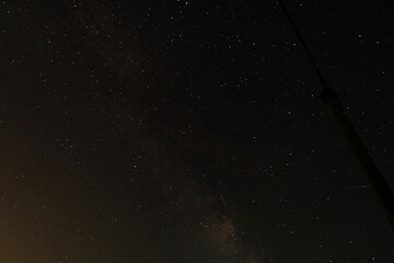 Long-exposure panorama shows the Milky Way and faint meteors streaking across dark rural sky,...