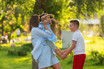 Mother and older son hoist a giggling little girl between them in a golden evening park, enjoying...