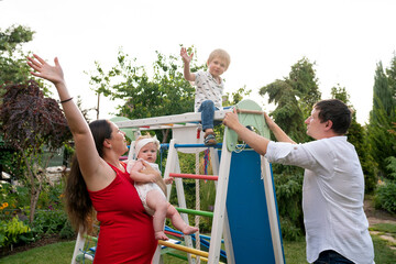 Mother with baby and father support while their son waves from the top of colorful backyard...