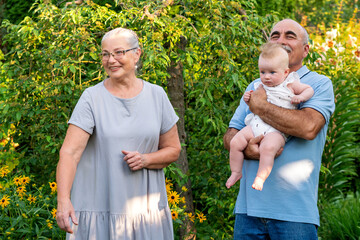 Grandparents warmly hold their baby and toddler outdoors in a lush garden, capturing joyful...