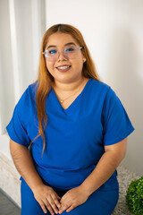 Young nurse smiling wearing blue scrubs and glasses