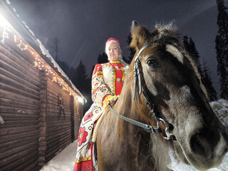 Beautiful Russian girl in traditional dress poses with horse during Maslenitsa celebration in winter