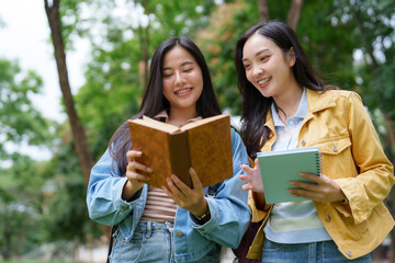 Two smiling university students reading a book together outdoors