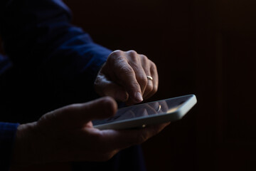 Mature man hands using a mobile phone against a dark background 