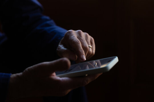 Mature man hands using a mobile phone against a dark background 