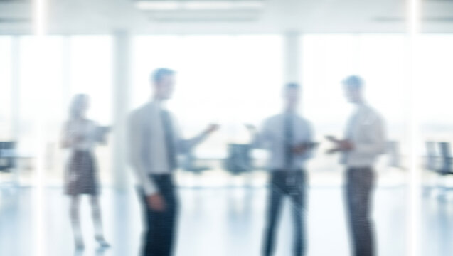 Blurred figures of people in business attire stand in a bright office space.