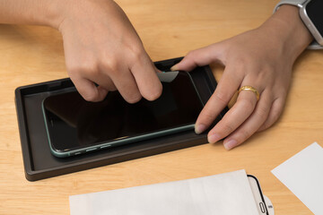 Close up of hands installing screen protector on smartphone using tool for clean alignment on...