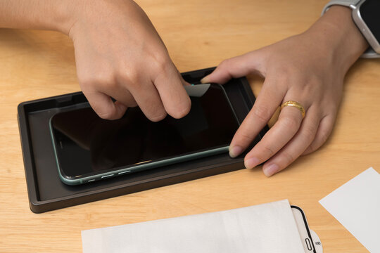Close up of hands installing screen protector on smartphone using tool for clean alignment on wooden desk