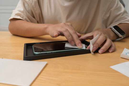 Hand cleaning smartphone screen with wet wipe before installing screen protector on wooden table surface - Powered by Adobe