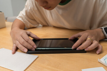 Person closely inspecting smartphone while installing tempered glass screen protector on wooden surface