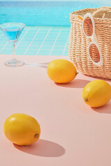 A peaceful poolside with woven basket, sunglasses, lemons, and blue cocktail on pastel flooring. The turquoise water and sky highlight the fresh summer vibe.