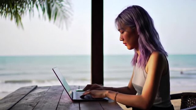 A woman with purple hair works on a laptop, enjoying the beach view. - Powered by Adobe
