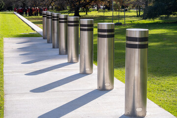 Row of stainless steel security bollards installed along a pedestrian path in a public park in...