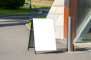 Blank A-frame sidewalk sign with mockup copy space placed near a modern building entrance....