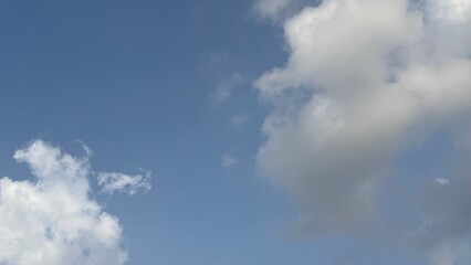 Fluffy white clouds softly drift across a clear blue sky creating a serene atmosphere
